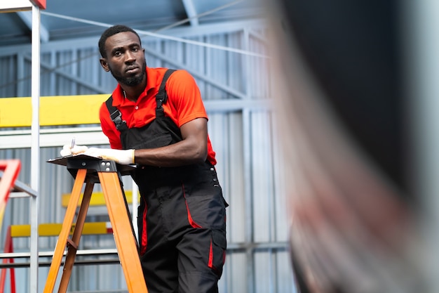 Black male mechanic choose car tire at a tire store. Expertise mechanic working in automobile repair garage.