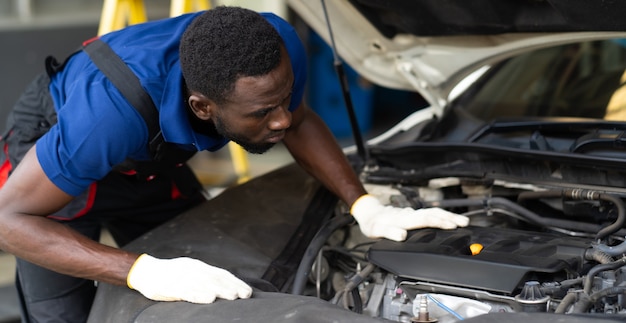 Black male mechanic repairs car in  garage. Car maintenance and auto service garage concept.