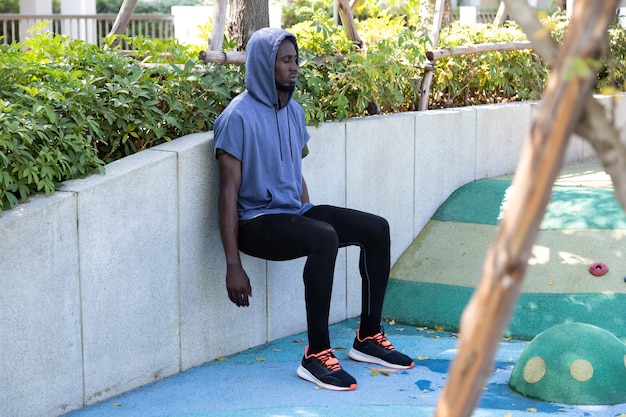 Black Male runner doing stretching exercise beside road in park at autumn morning. checking performance or heart rate pulse trace. Sport and fitness outdoors