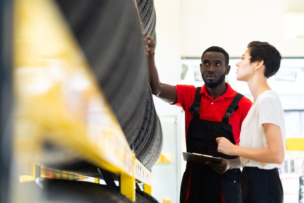 Black male salesman showing wheel tires to caucasian woman customer at car repair service and auto store shop.