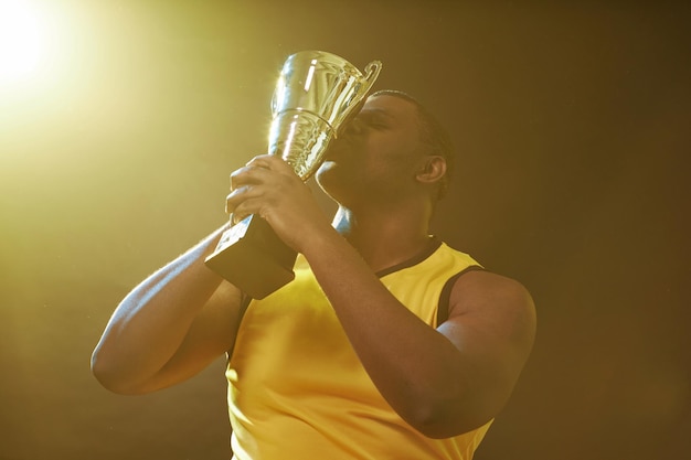 Чернокожий спортсмен целует трофей и празднует победу.