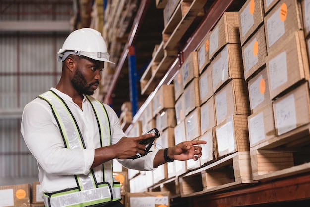 Foto personale di sesso maschile nero che utilizza uno scanner di codici a barre digitale che lavora controllando le scorte nel magazzino logistico