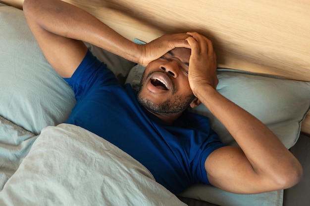 Foto uomo nero risveglio sbadigliando e strofinando gli occhi sdraiato in camera da letto