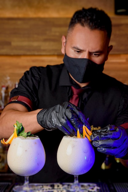 Barista uomo nero con maschera che prepara un cocktail. concetto di bevande