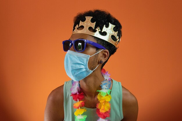 Black man in costume for carnival with pandemic mask isolated on orange background