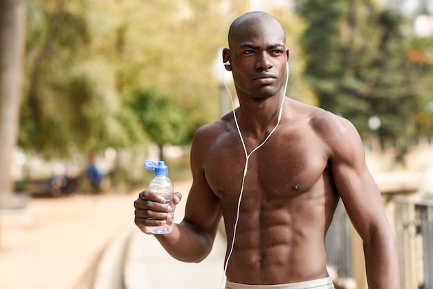 Black man drinking water after running in urban background.