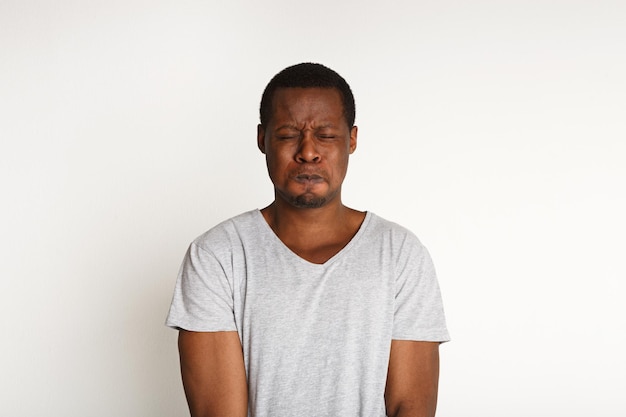 Black man expressing fear and disgust on face, grimacing on white studio background. Negative emotions