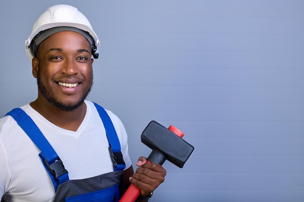 Black man in a hard hat and work clothes looks at the camera