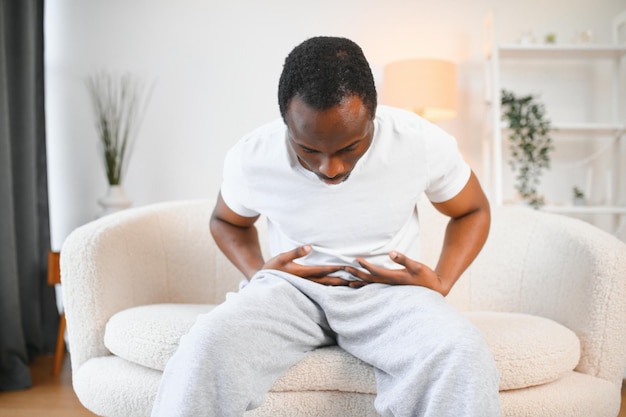 Photo black man having stomachache suffering from painful abdominal spasm standing touching aching abdomen at home