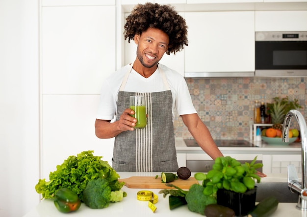 キッチンで緑の野菜ジュースのガラスを保持している黒人男性