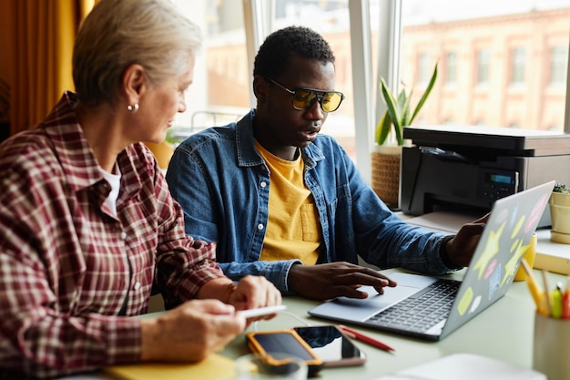 black man instructing senior colleague on proper use of computer at desk in office