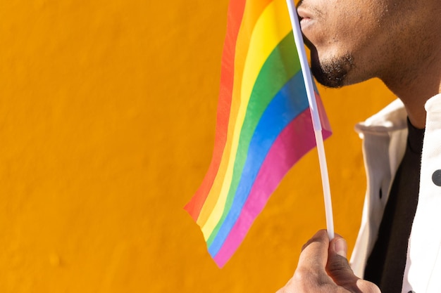 Black Man kissing a rainbow lgtb flag next to a yellow wall on the background