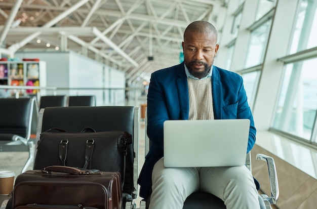 Photo black man laptop and luggage at airport for business travel trip or working while waiting to board plane african american male at work on computer checking online schedule times for flight delay