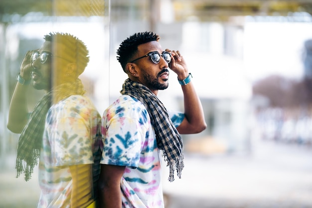 Black man leaning against a glass wall holding his sunglasses