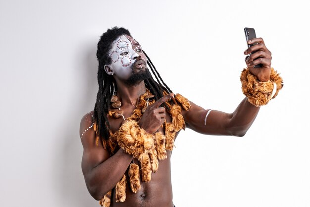 L'uomo di colore guarda il telefono cellulare parlando, prendendo foto isolato sopra il muro bianco