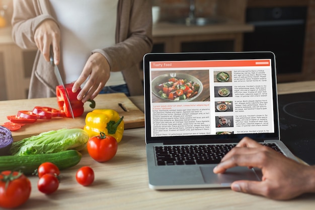 Black man looking at recipe in laptop while woman cutting pepper. Family preparing dinner together