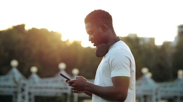 Черный мужчина смотрит на экран смартфона на заднем солнечном свете