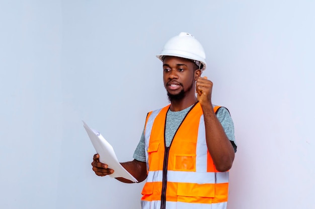 A black man in an orange vest holds a piece of paper and shows a gesture of power.