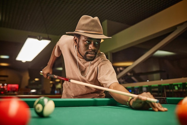 Photo black man playing pool and hitting ball with cue stick in pool club