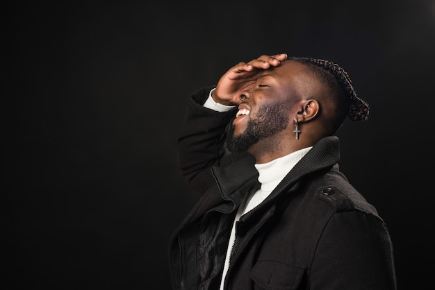 Black man in profile laughing with his hand on his face. Close up. Black background.