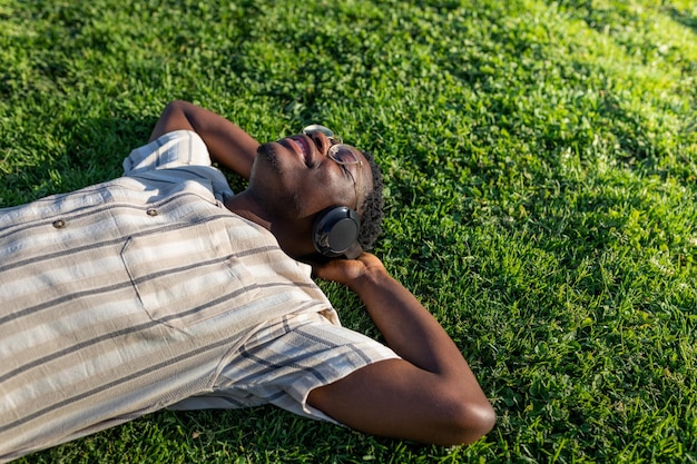 Black man relaxing outdoors Happy black male lying on grass listening to music with headphones Copy space