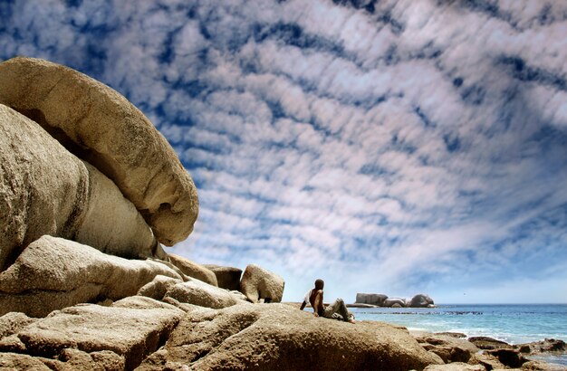 Black man seated on sea rocks looking sea 