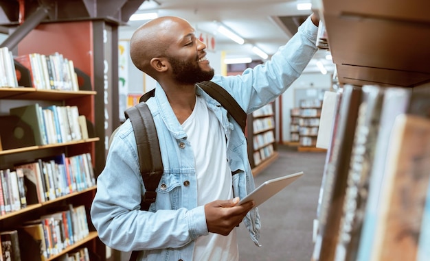 Black man student and library bookshelf of a university college and knowledge center Notebook happy young person and smile of a male with books for learning and study research info at school