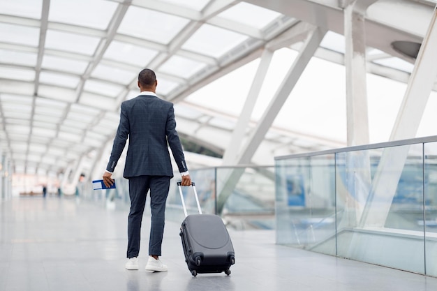 공항 터미널 후면 보기에서 짐을 들고 걷는 정장을 입은 흑인