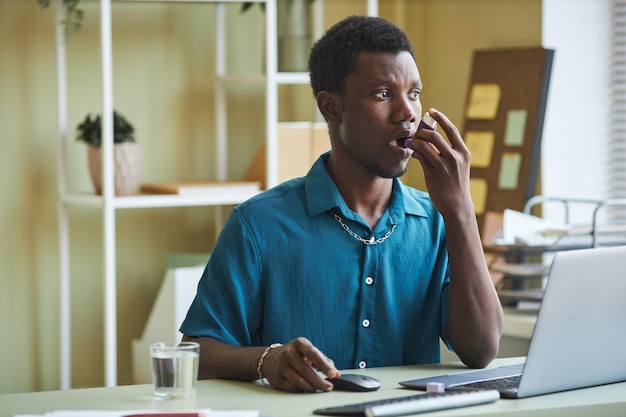 Черный мужчина использует ингалятор от астмы на рабочем месте в офисе