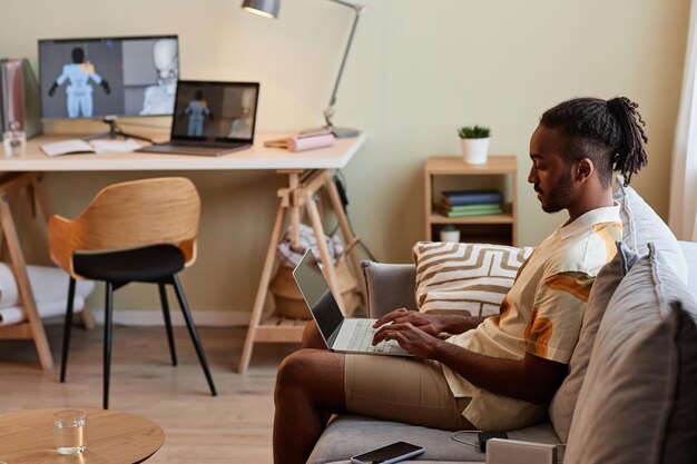 Black man using laptop while sitting on sofa