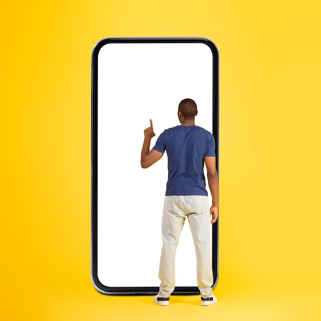 Black man using phone standing back to camera yellow background