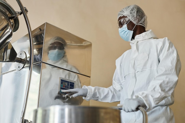 Black man wearing protective suit in factory workshop and pressing buttons