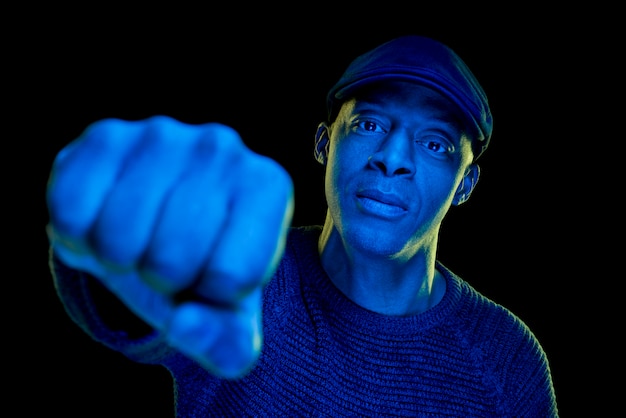 Black man with blue light wearing a flat cap, isolated on black background.