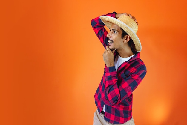 Black Man With Junina Party Outfit Isolated on Orange Background Young man wearing traditional clothes for Festa Junina Brazilian June festival