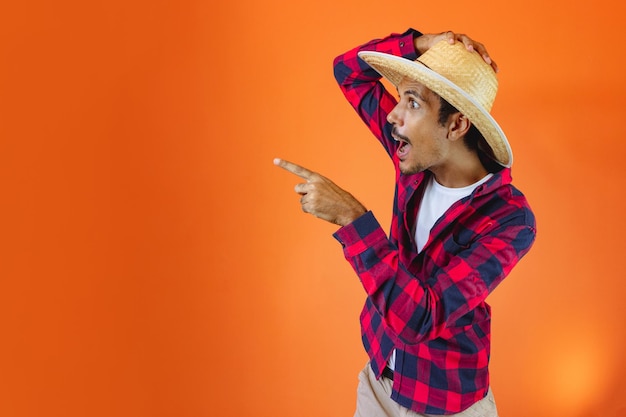 Black Man With Junina Party Outfit Pointing on Isolated on Orange Background Young man wearing traditional clothes for Festa Junina Brazilian June festival