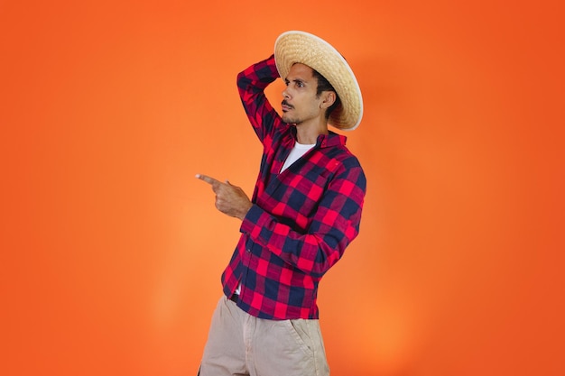 Black Man With Junina Party Outfit Pointing Isolated on Orange Background Young man wearing traditional clothes for Festa Junina Brazilian June festival