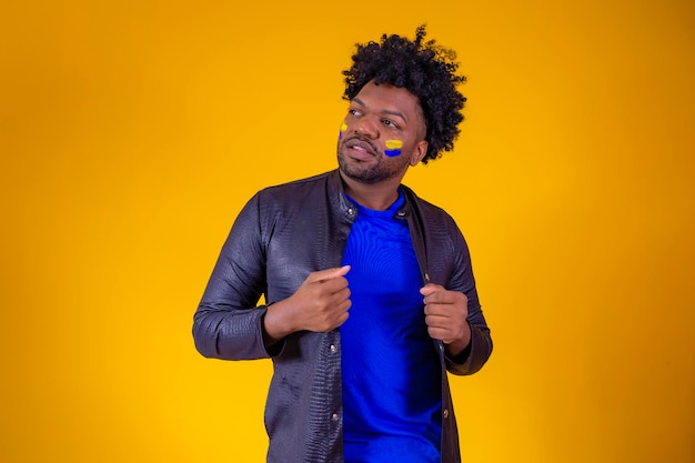 Black man on yellow background with his face painted with blue and yellow colors showing off to the camera