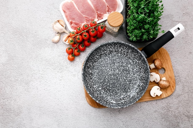 Black marble frying pan with products on grey table background top view