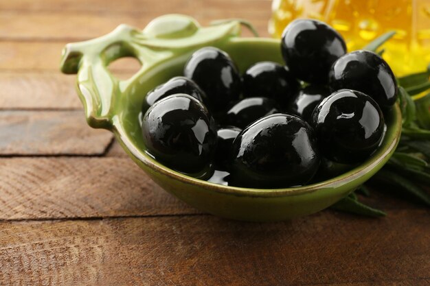 Photo black marinated olives in small green saucepan with oil near branch and oilcan on rustic wooden background