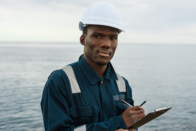 Black maritime worker making notes near sea