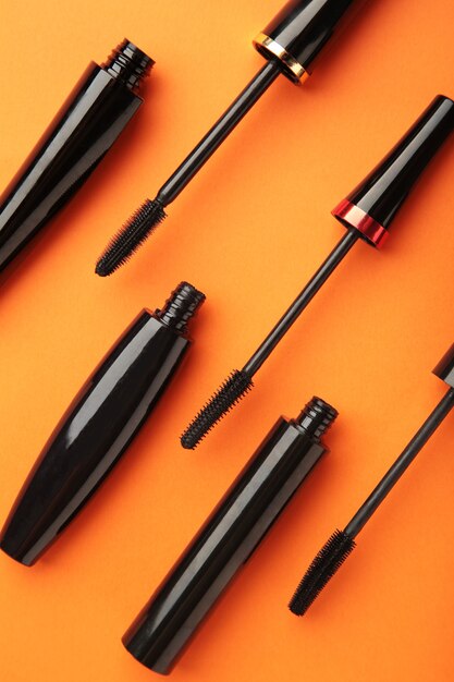 Black mascara wand and tube on orange background. Vertical photo