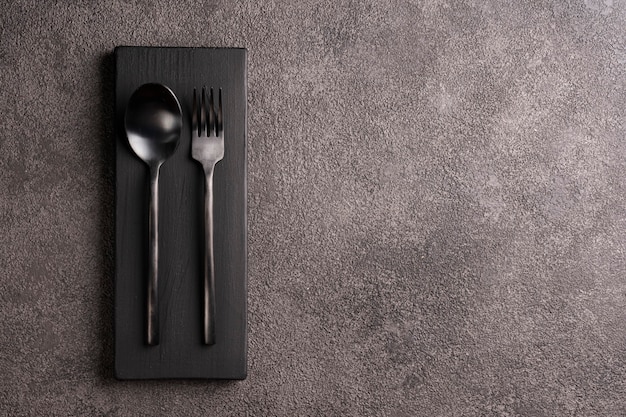Black matte spoon and fork. Minimalistic set, copyspace for a restaurant or cafe menu against a dark concrete table. 