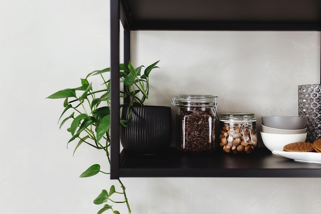 Black metal shelves in the kitchen on a gray concrete wall in a loft style. Green flowerpots.