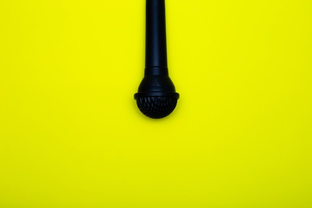 A black microphone hangs from above on a yellow background