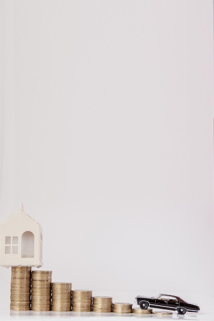 A black model of a car and house with coins in the form of a histogram on a white background Concept of lending savings insurance