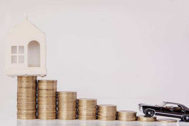 A black model of a car and house with coins in the form of a histogram on a white background Concept of lending savings insurance