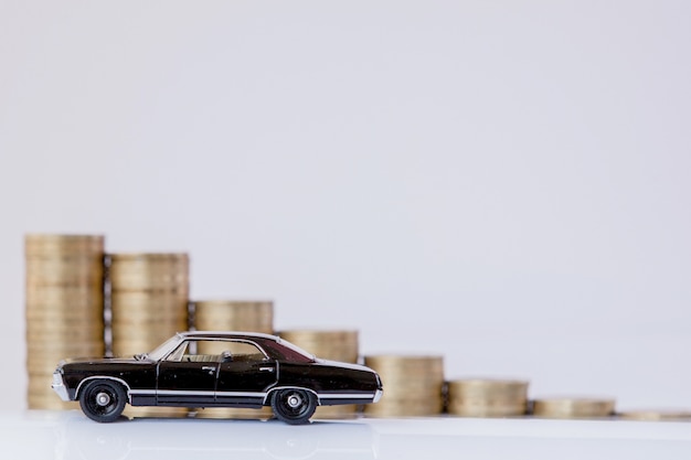 Photo a black model of a car with coins in the form of a histogram on a white background. concept of lending, savings, insurance.