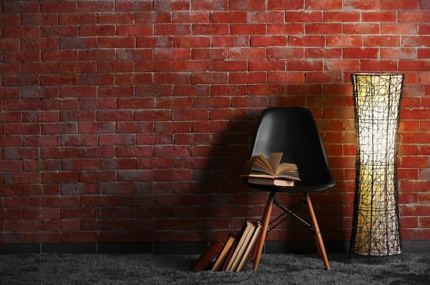 벽돌 벽 배경에 램프와 책이 있는 검은색 현대 의자