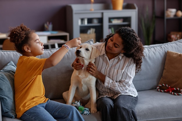 Photo black mother and daughter playing with cute puppy on sofa at home
