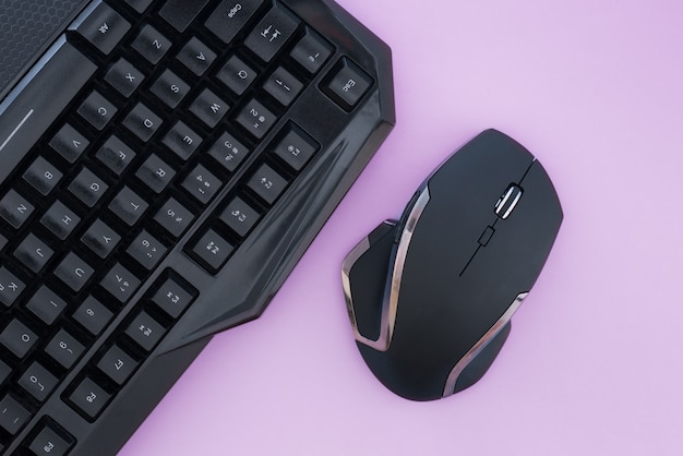 Black mouse and keyboard on a pink background, top view. Workplace, mouse and keyboard flat lay